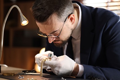 Photo of Appraiser with loupe evaluating luxury wristwatch at table indoors