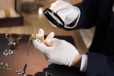 Photo of Appraiser with magnifying glass evaluating luxury wristwatch at table indoors, closeup