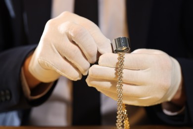 Photo of Appraiser with loupe evaluating luxury jewelry at table, closeup