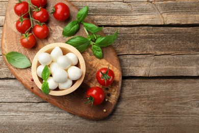 Photo of Tasty mozzarella cheese balls in bowl, basil, peppercorns and tomatoes on wooden table, top view. Space for text