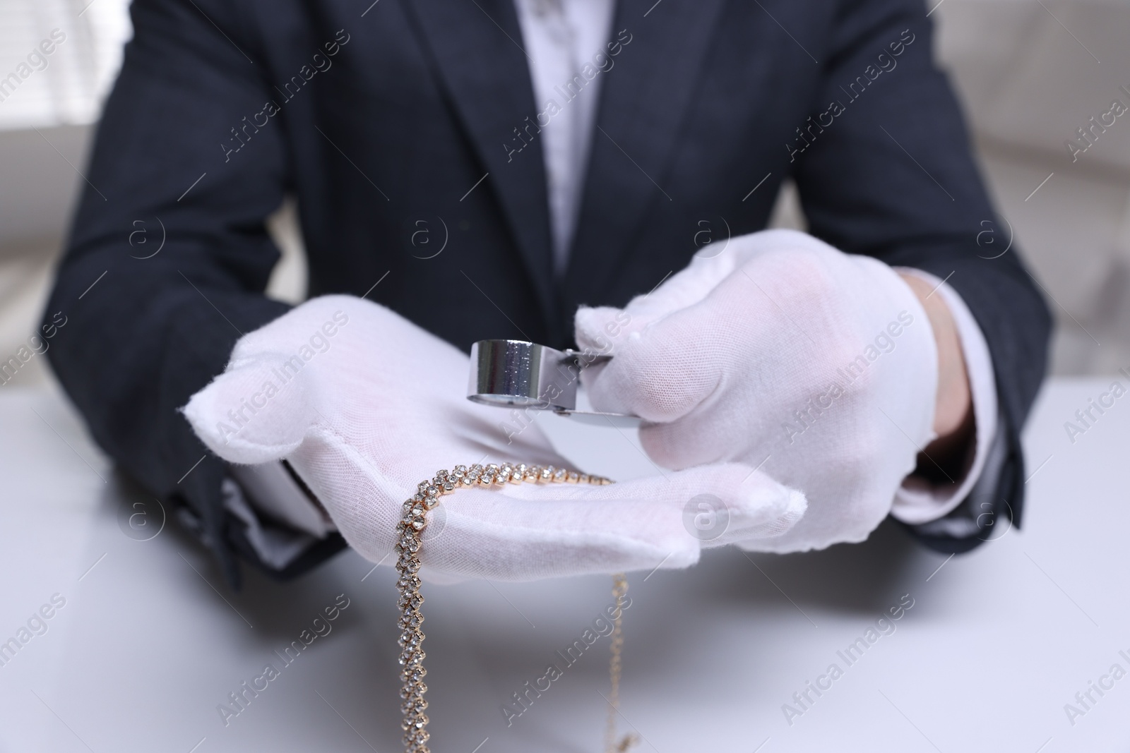 Appraiser evaluating luxury necklace at white table indoors, closeup Photo of Appraiser evaluating luxury necklace at white table indoors, closeup