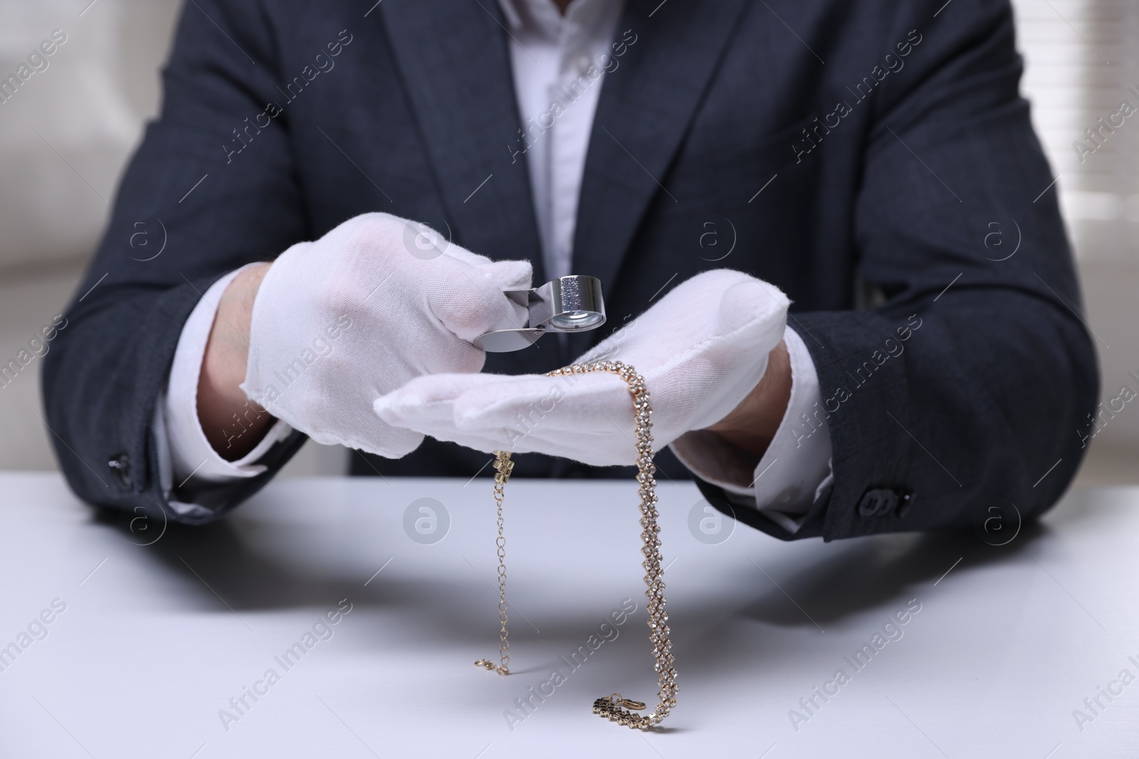 Appraiser evaluating luxury necklace at white table indoors, closeup Photo of Appraiser evaluating luxury necklace at white table indoors, closeup