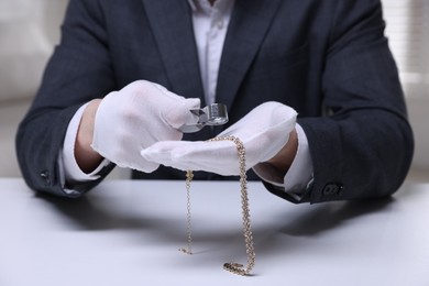 Photo of Appraiser evaluating luxury necklace at white table indoors, closeup