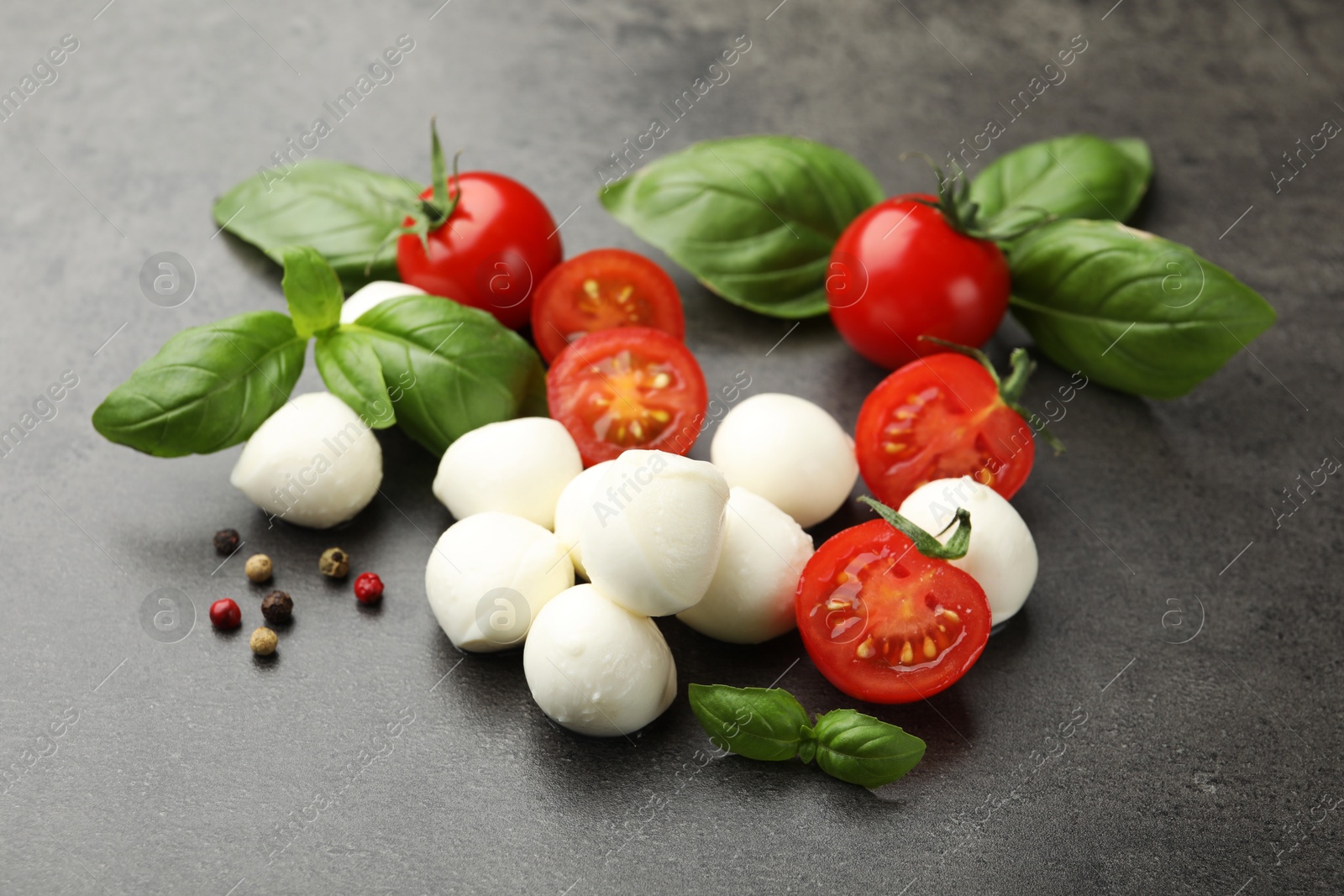 Mozzarella cheese, tomatoes, basil and peppercorns on grey table Photo of Mozzarella cheese, tomatoes, basil and peppercorns on grey table