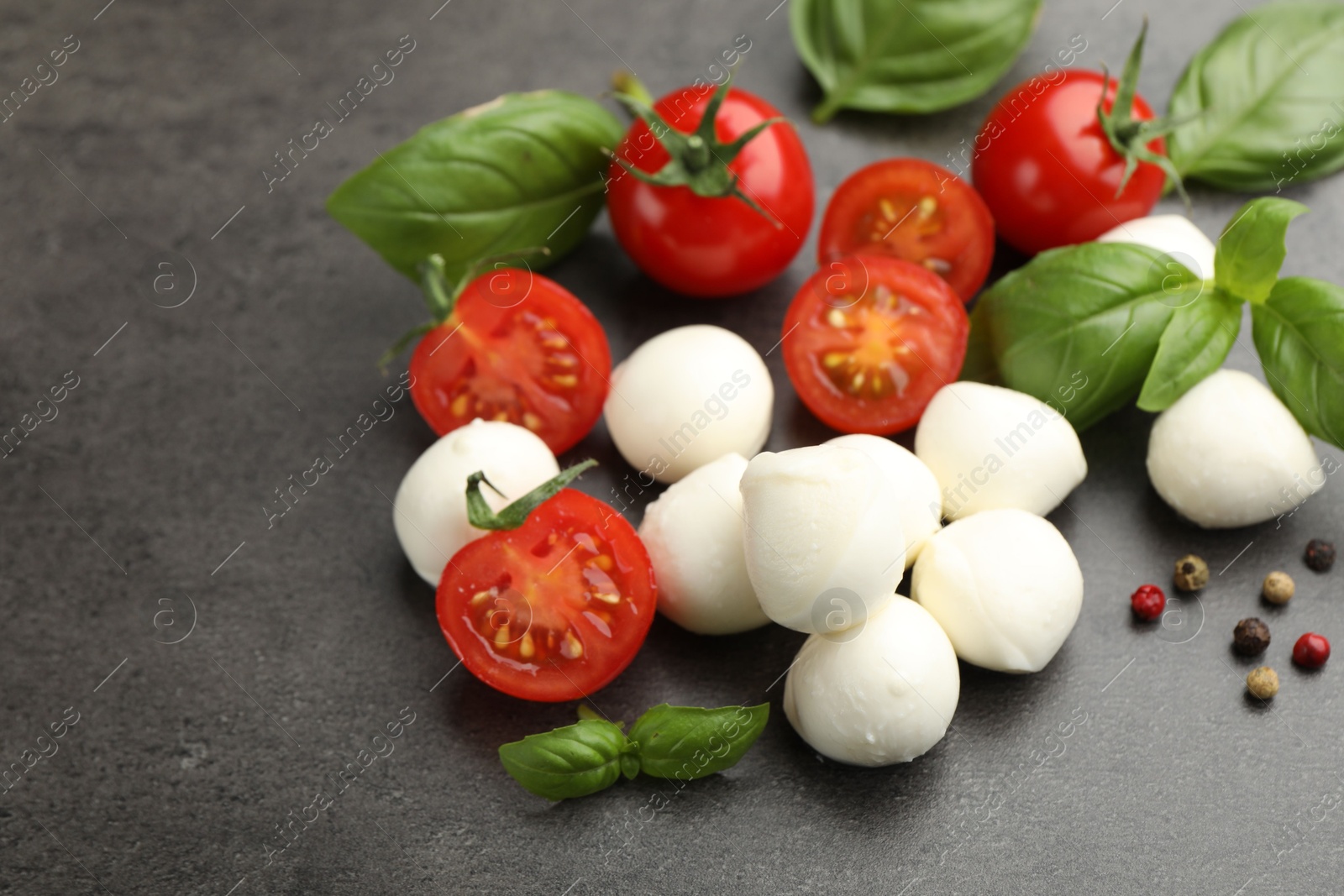 Mozzarella cheese, tomatoes, basil and peppercorns on grey table, closeup Photo of Mozzarella cheese, tomatoes, basil and peppercorns on grey table, closeup