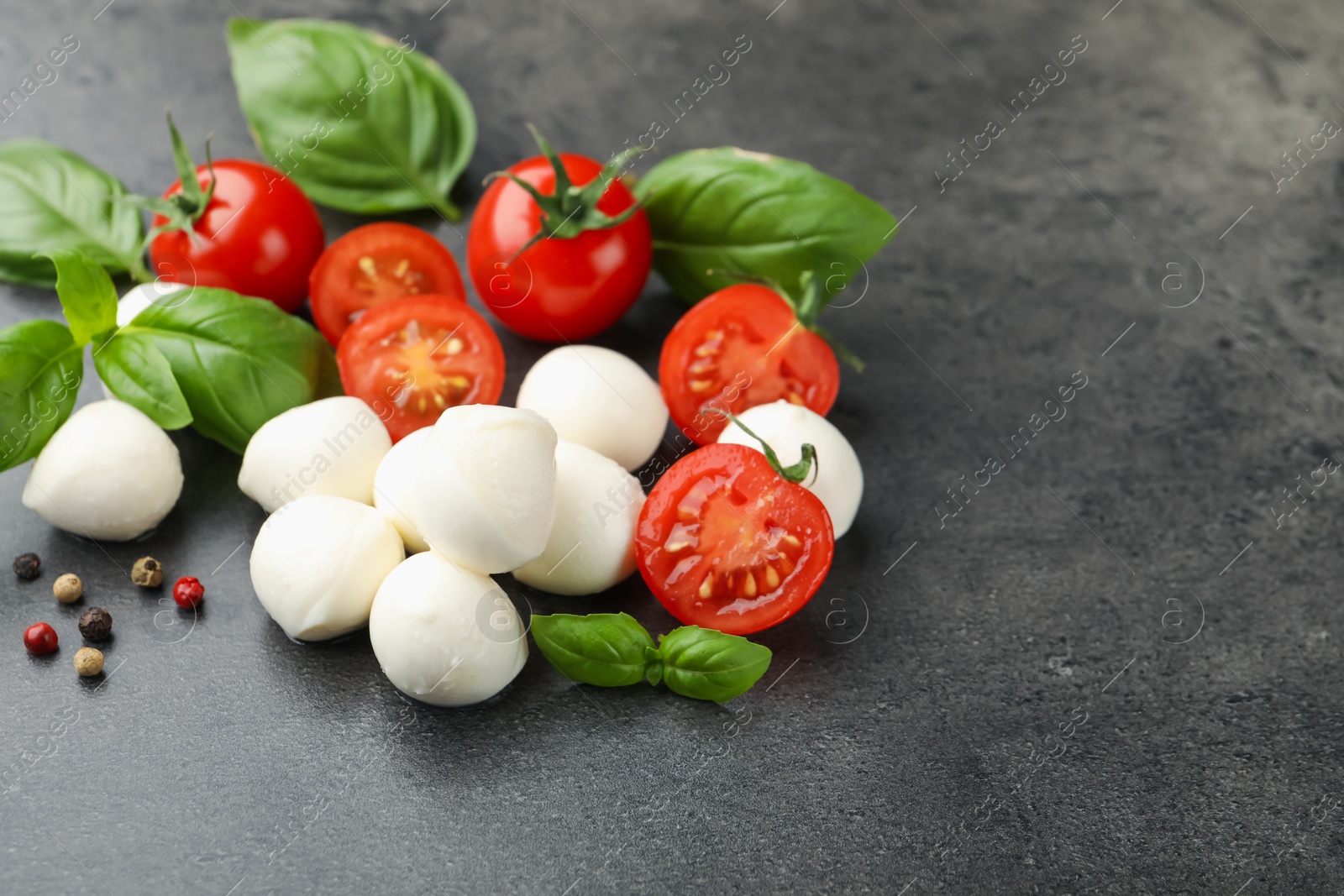 Mozzarella cheese, tomatoes, basil and peppercorns on grey table, closeup Photo of Mozzarella cheese, tomatoes, basil and peppercorns on grey table, closeup