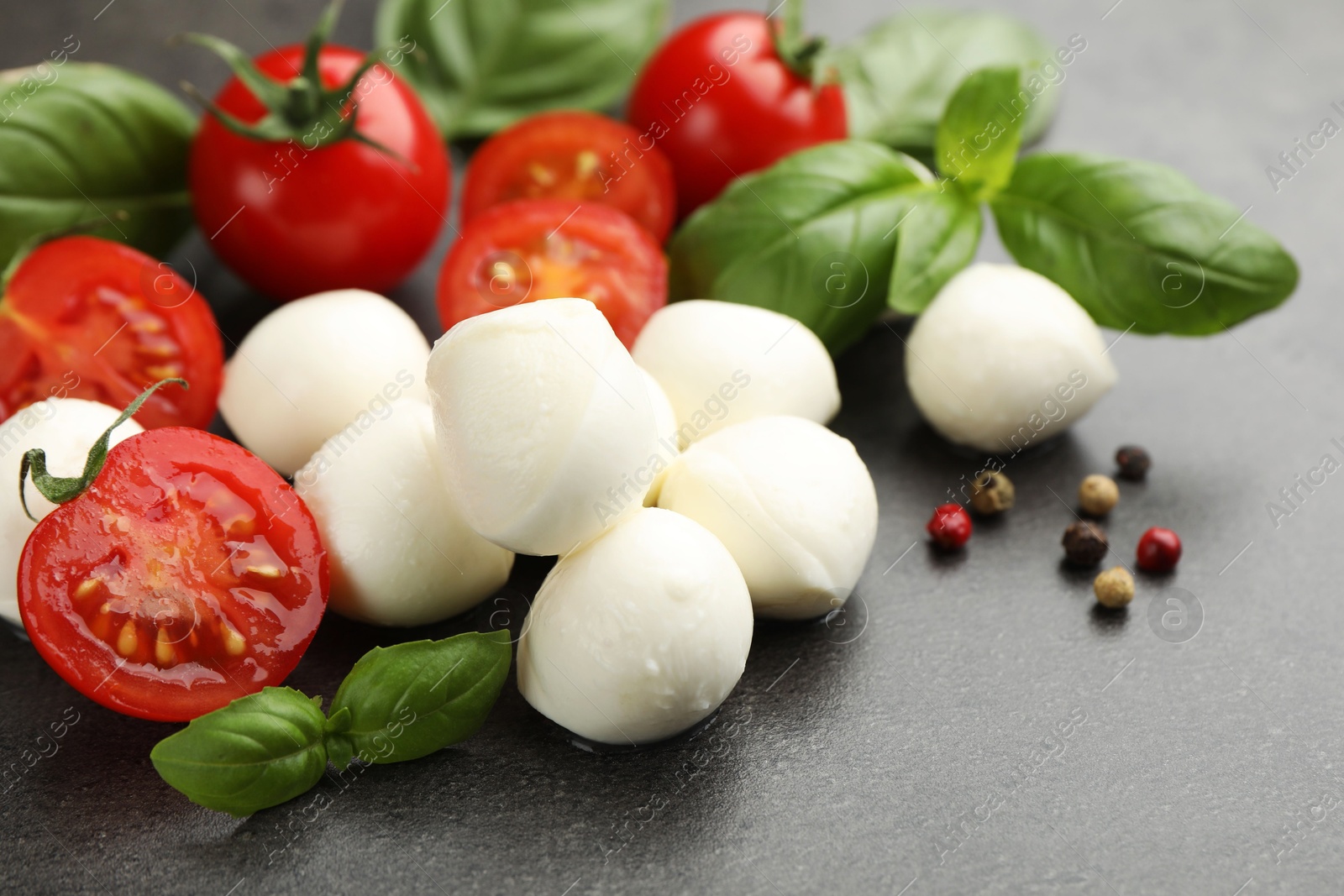 Mozzarella cheese, tomatoes, basil and peppercorns on grey table, closeup Photo of Mozzarella cheese, tomatoes, basil and peppercorns on grey table, closeup