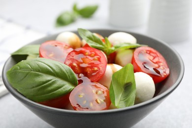 Photo of Tasty salad with mozzarella, tomatoes and basil on light table, closeup