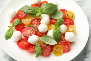 Photo of Tasty salad with mozzarella, tomatoes and basil on white marble table, closeup