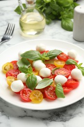 Photo of Tasty salad with mozzarella, tomatoes and basil on white marble table, closeup