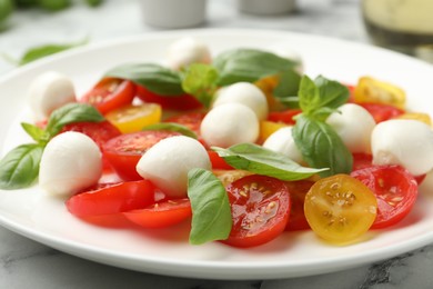 Photo of Tasty salad with mozzarella, tomatoes and basil on white marble table, closeup