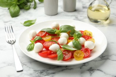 Photo of Tasty salad with mozzarella, tomatoes and basil served on white marble table, closeup