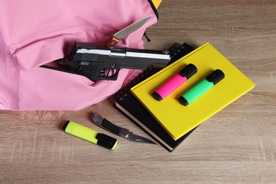 Photo of Backpack with gun, knife and stationery on wooden table, closeup