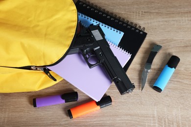 Photo of Backpack with gun, knife and stationery on wooden table, above view