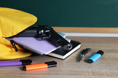 Photo of Backpack with gun, knife and stationery on wooden table, closeup