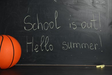 Photo of Phrases School Is Out and Hello Summer with exclamation mark on blackboard. Basketball ball and chalk on black wooden table