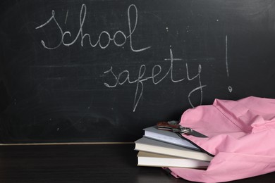 Photo of Backpack with knife and books on black wooden table near blackboard. School safety