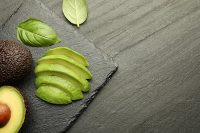 Photo of Tasty ripe green avocados and basil on black table, flat lay. Space for text