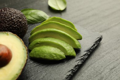 Photo of Tasty ripe green avocados and basil on black table, closeup