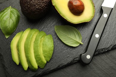 Photo of Tasty ripe green avocados, basil and knife on black table, flat lay