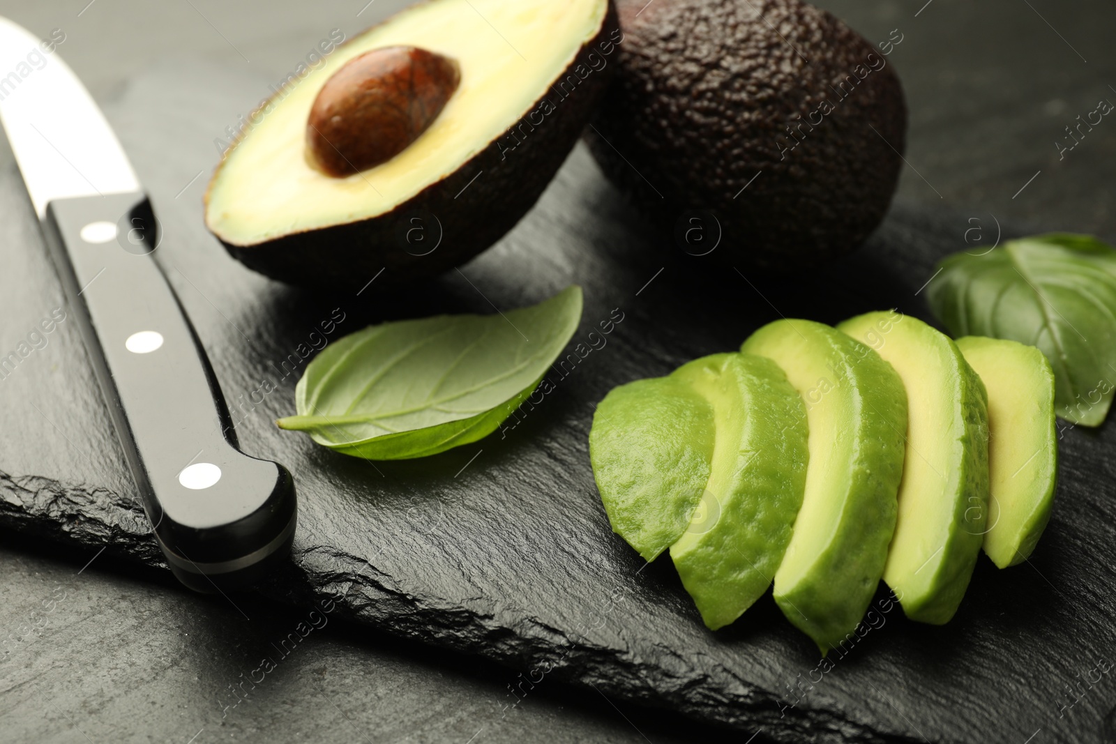 Tasty ripe green avocados, basil and knife on black table, closeup Photo of Tasty ripe green avocados, basil and knife on black table, closeup