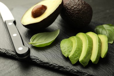 Photo of Tasty ripe green avocados, basil and knife on black table, closeup