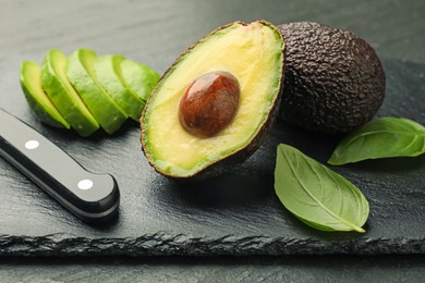 Photo of Tasty ripe green avocados, basil and knife on black table, closeup