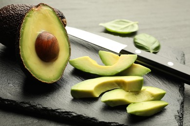 Photo of Tasty ripe green avocados, basil and knife on table, closeup