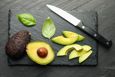 Photo of Tasty ripe green avocados, basil and knife on black table, flat lay