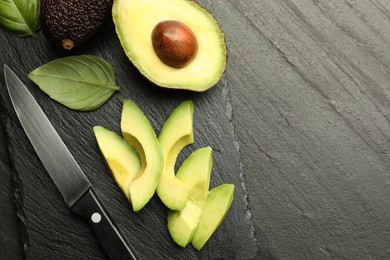 Photo of Tasty ripe green avocados, basil and knife on black table, flat lay. Space for text