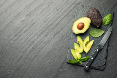 Photo of Tasty ripe green avocados, basil and knife on black table, flat lay. Space for text