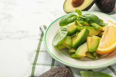 Photo of Tasty ripe green avocados, basil and lemon on white marble table, closeup. Space for text