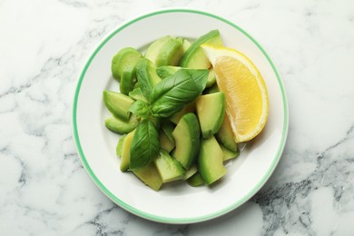 Photo of Tasty ripe green avocado, basil and lemon on white marble table, top view