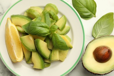 Photo of Tasty ripe green avocados, basil and lemon on white marble table, flat lay