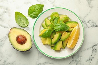 Photo of Tasty ripe green avocados, basil and lemon on white marble table, flat lay