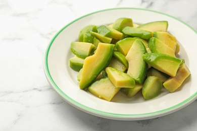 Photo of Cut ripe green avocado on white marble table, closeup