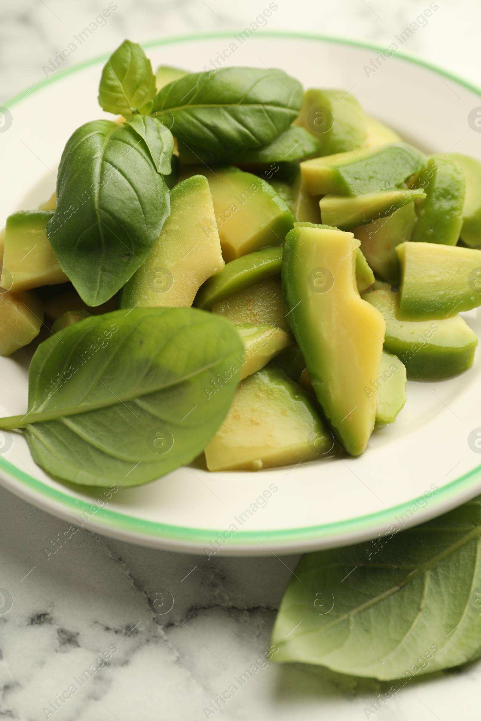Cut ripe green avocado and basil on white marble table, closeup Photo of Cut ripe green avocado and basil on white marble table, closeup