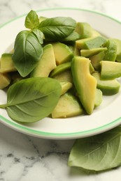 Photo of Cut ripe green avocado and basil on white marble table, closeup