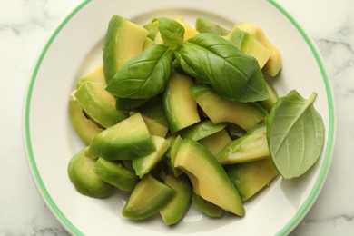 Photo of Cut ripe green avocado and basil on white marble table, top view