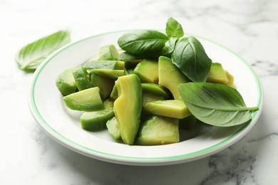 Photo of Cut ripe green avocado and basil on white marble table, closeup