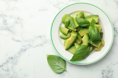 Photo of Cut ripe green avocado and basil on white marble table, top view. Space for text