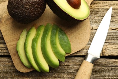 Photo of Tasty ripe green avocados and knife on wooden table, flat lay
