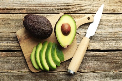 Photo of Tasty ripe green avocados and knife on wooden table, flat lay