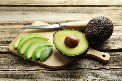Photo of Tasty ripe green avocados and knife on wooden table, closeup
