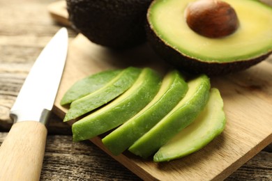 Photo of Tasty ripe green avocados and knife on wooden table, closeup