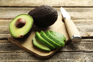 Photo of Tasty ripe green avocados and knife on wooden table, closeup