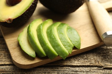 Photo of Tasty ripe green avocados and knife on wooden table, closeup