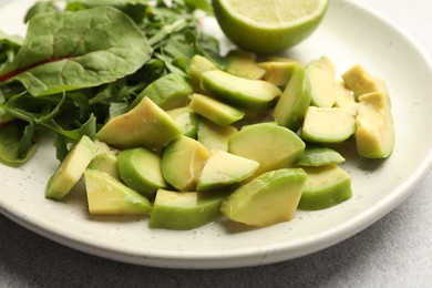 Photo of Cut ripe green avocado, greens and lime on light grey table, closeup