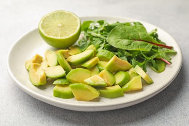 Photo of Cut ripe green avocado, greens and lime on light grey table, closeup