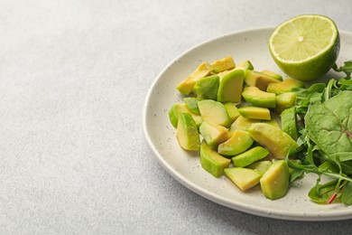 Photo of Cut ripe green avocado, greens and lime on light grey table, closeup. Space for text